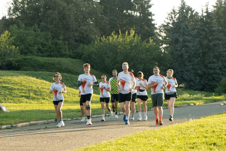 Group of runners wearing white shirts running along a park path with green grass and trees in the background.