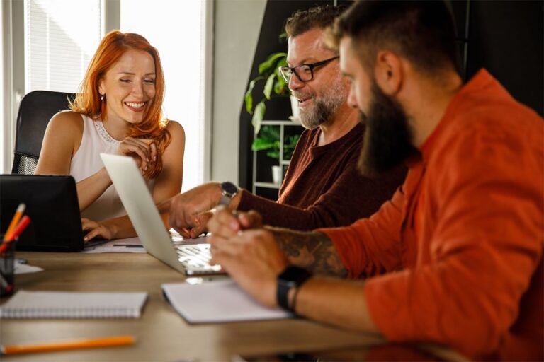 Tres profesionales de negocios revisando datos en un ordenador portátil, colaborando en estrategias de código, capital y cambio impulsadas por la ingeniería de inteligencia en un entorno moderno de servicios financieros.