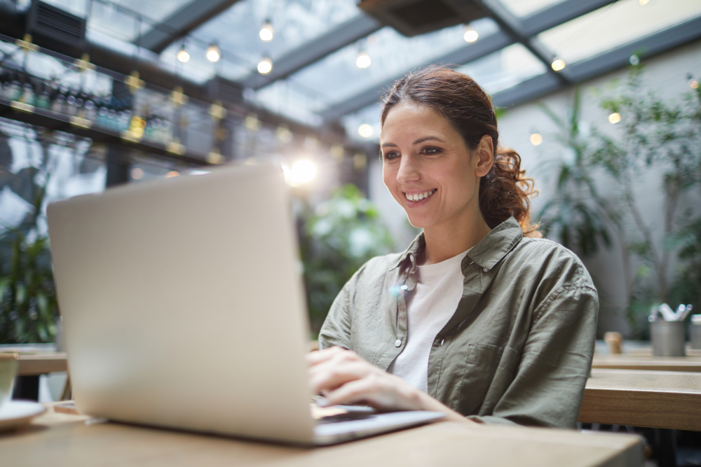 smiling-woman-using-laptop-cafe-e1685117147197