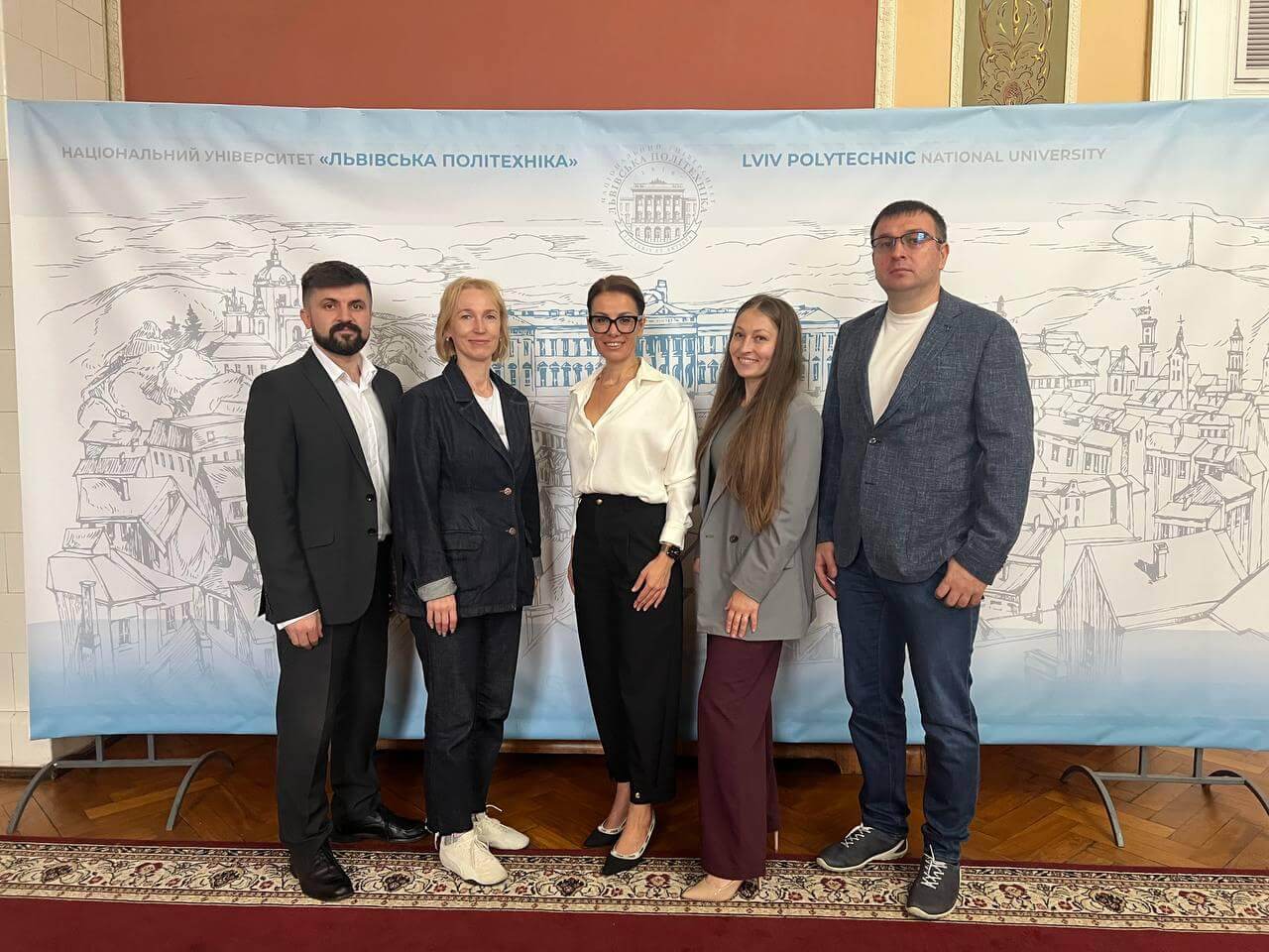 Five adults in business attire pose for a group photo in front of a banner for Lviv Polytechnic National University (Lviv Polytechnic).