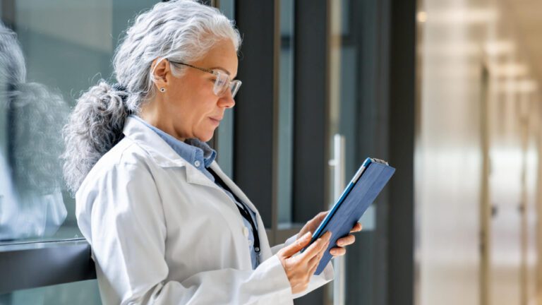 A woman doctor’s profile, looking down at a tablet.