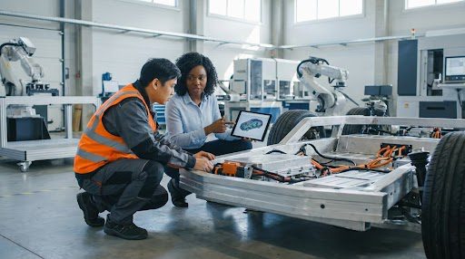 digital-engineers-collaborating - GlobalLogic Digital engineers collaborating in an industrial environment, interacting with a physical prototype and reviewing design data on a tablet, illustrating AI for physical systems, digital twin integration, and real-world deployment of embedded AI in manufacturing.