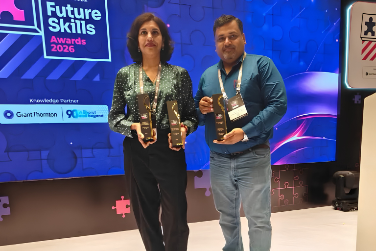 Two people on stage holding awards at the Future Skills Awards 2026 ceremony with a blue backdrop behind them.