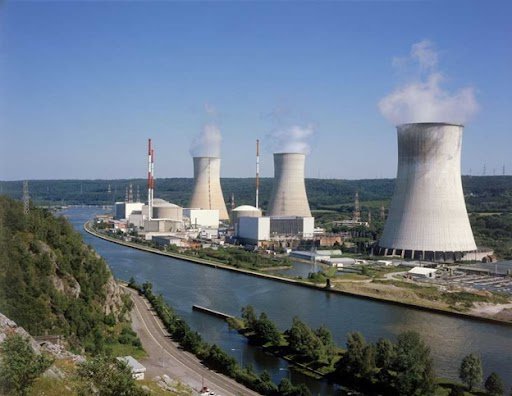 Industrial power plant with tall cooling towers emitting steam beside a river.