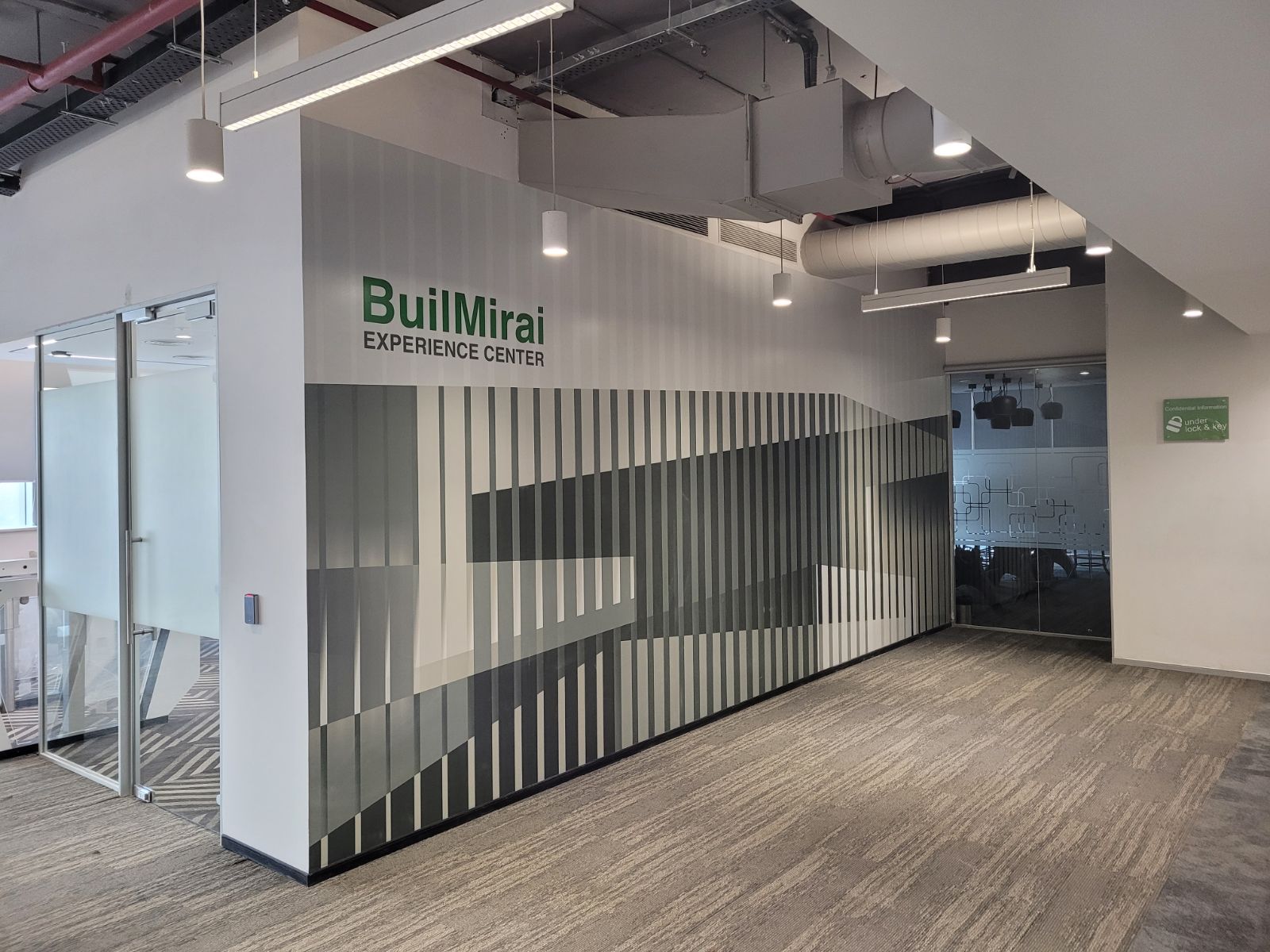 Wall graphic reading 'BuilMirai EXPERIENCE CENTER' with a gray vertical-stripe mural in a modern office lobby.