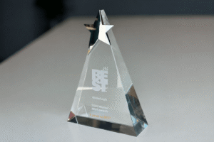 IMG_9779 - GlobalLogic Crystal pyramid trophy with 'BEST' inscription and logos, awarded by GlobalLogic for 2026 BEST Awards on a light desk surface.