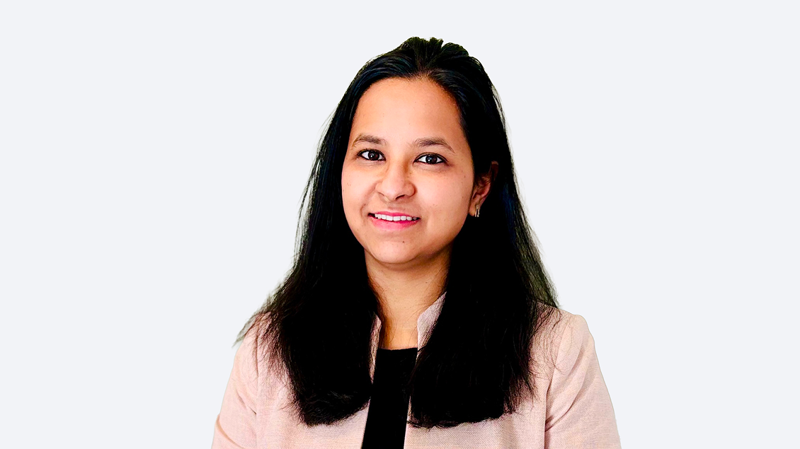 Professional headshot of a smiling woman with long black hair, wearing a light pink blazer against a pale background.