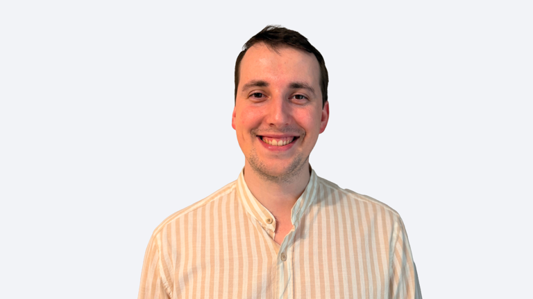 Smiling man in beige striped button-down shirt facing the camera against a light gray backdrop