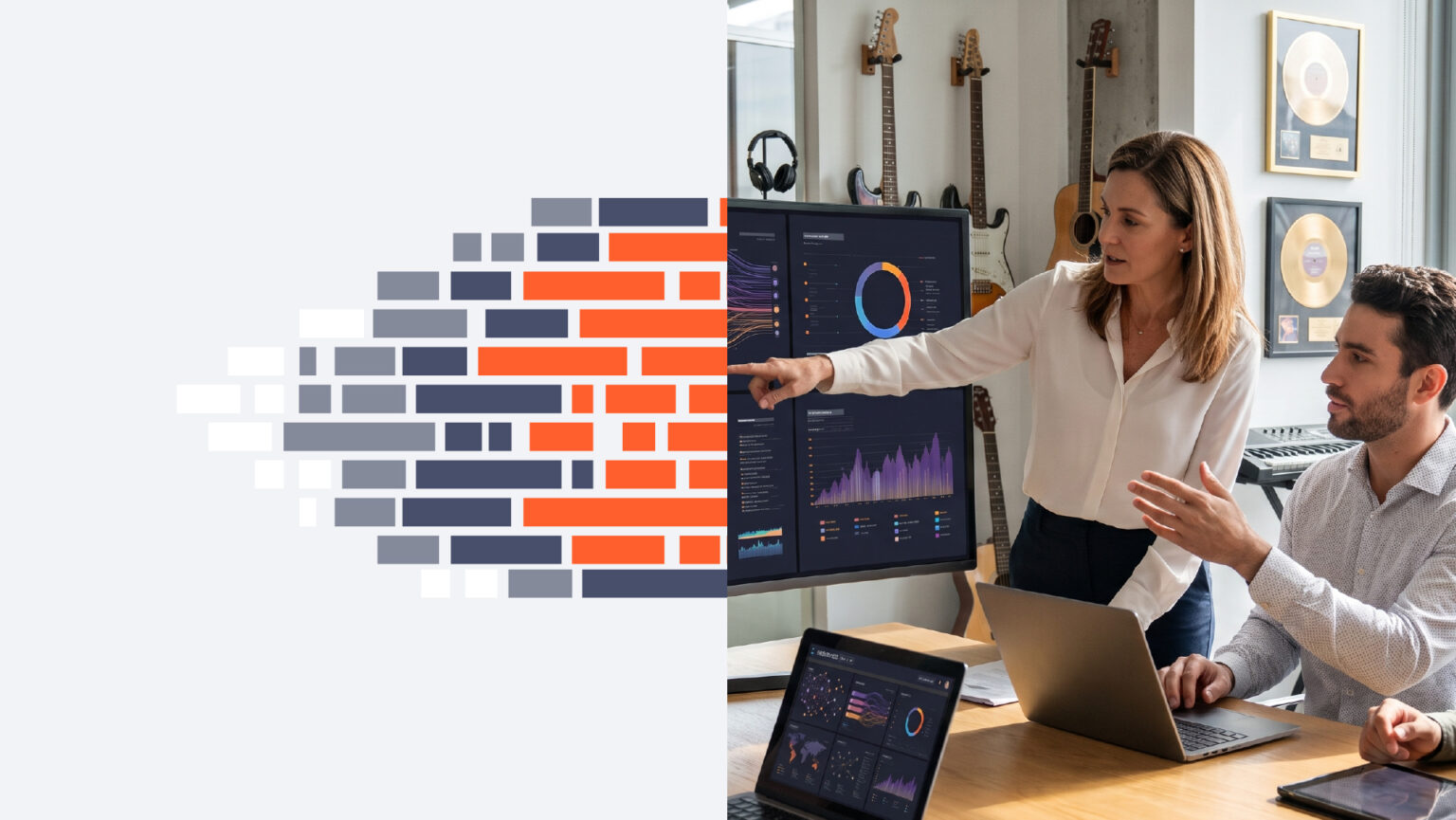 Two professionals discuss data on a large monitor showing charts and graphs in a bright office space.