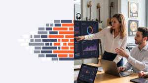 Two professionals discuss data on a large monitor showing charts and graphs in a bright office space.
