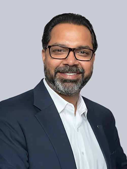 Professional headshot of a smiling man with dark hair and glasses, wearing a navy blazer and white shirt against a light gray background.